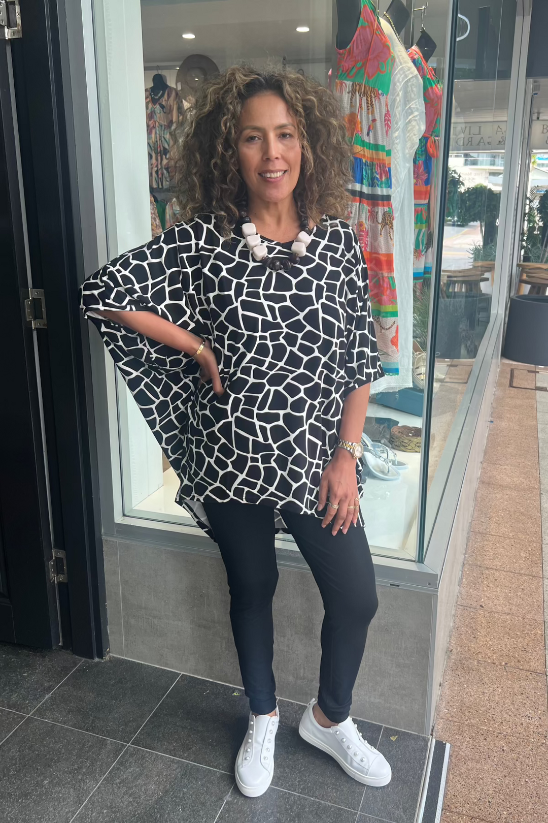A person wearing black bamboo leggings with a wide waistband, paired with white sneakers. The leggings feature a patterned design.