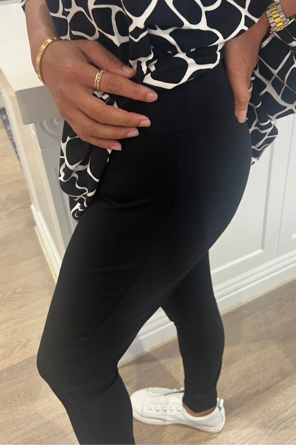A person wearing black bamboo leggings with a wide waistband, paired with white sneakers. The leggings feature a patterned design.