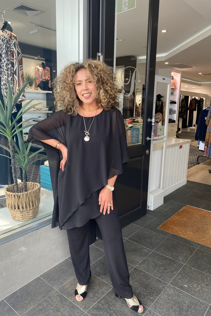 Woman in a black outfit standing outside a store with clothing displayed inside.