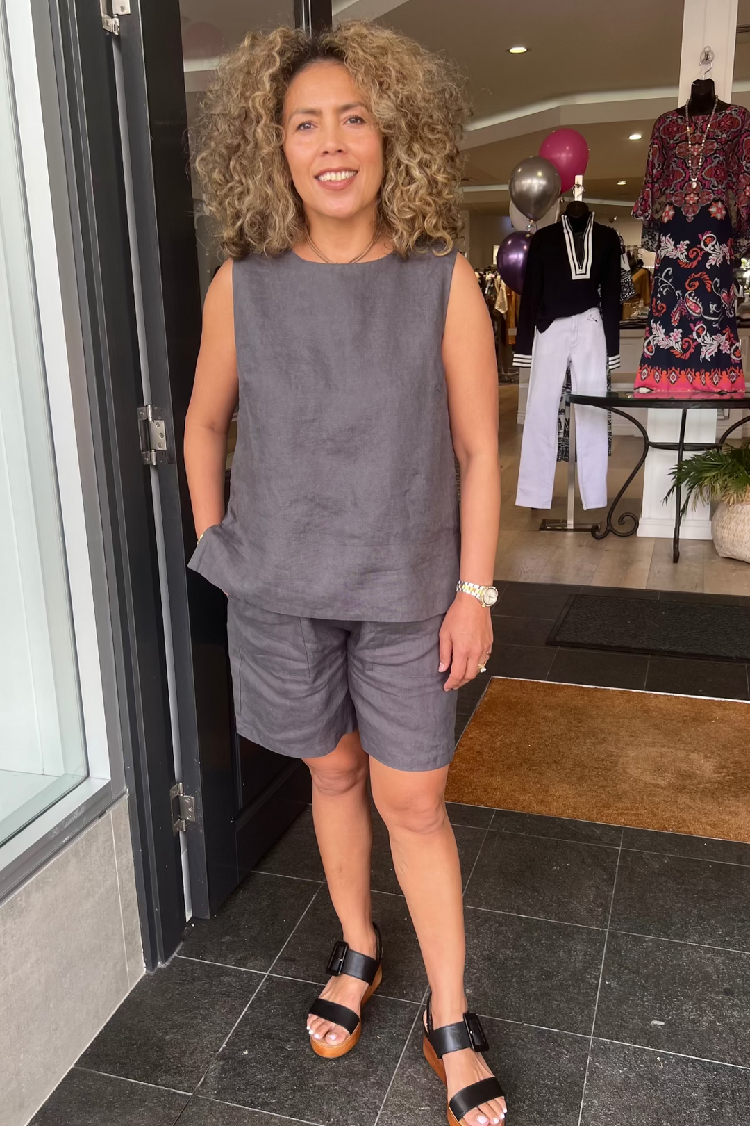 Woman in gray sleeveless top and shorts standing in a store entrance.