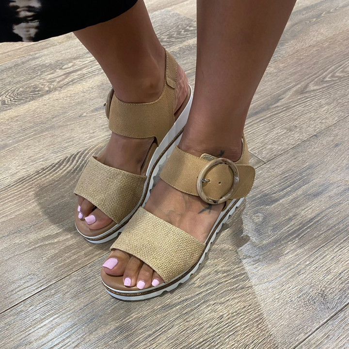 Beige sandals worn on a wooden floor