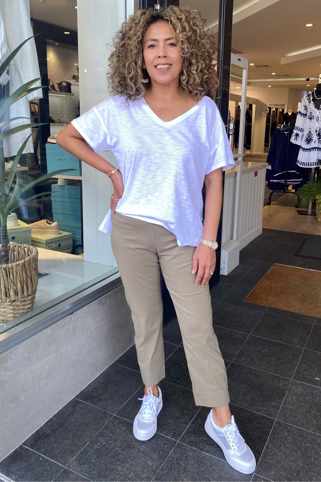 Woman standing in a store with a white shirt and beige pants, smiling.