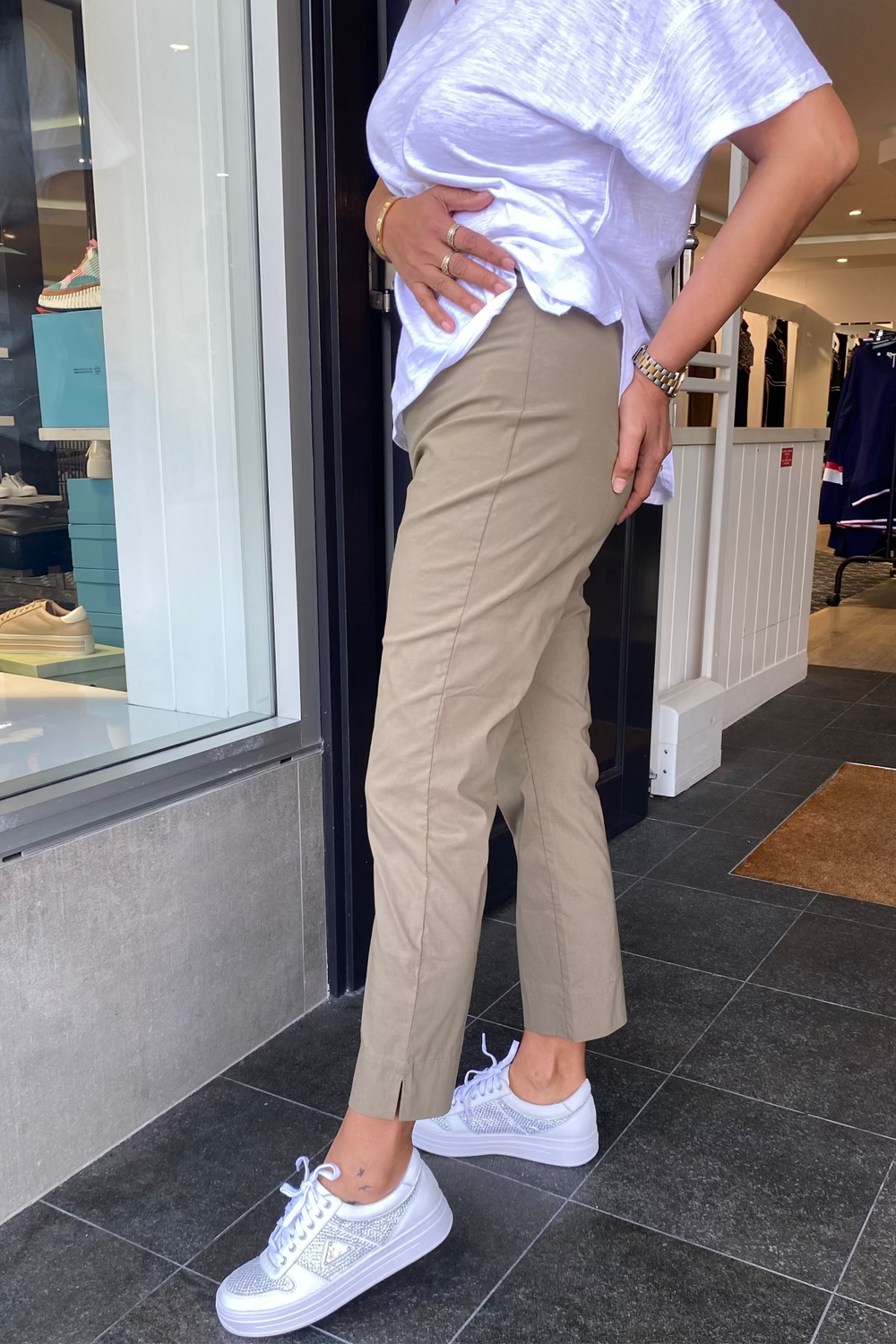 Person wearing a white top, beige pants, and white sneakers standing on a tiled floor.