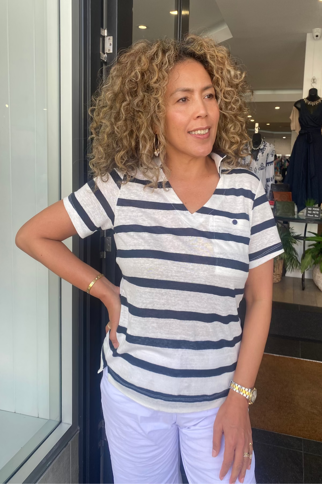 Woman wearing a striped shirt and white pants standing in front of a store window.