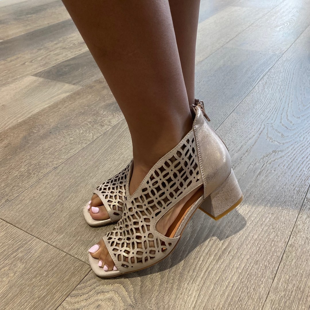 Beige open-toe sandals with cut-out design worn on a wooden floor