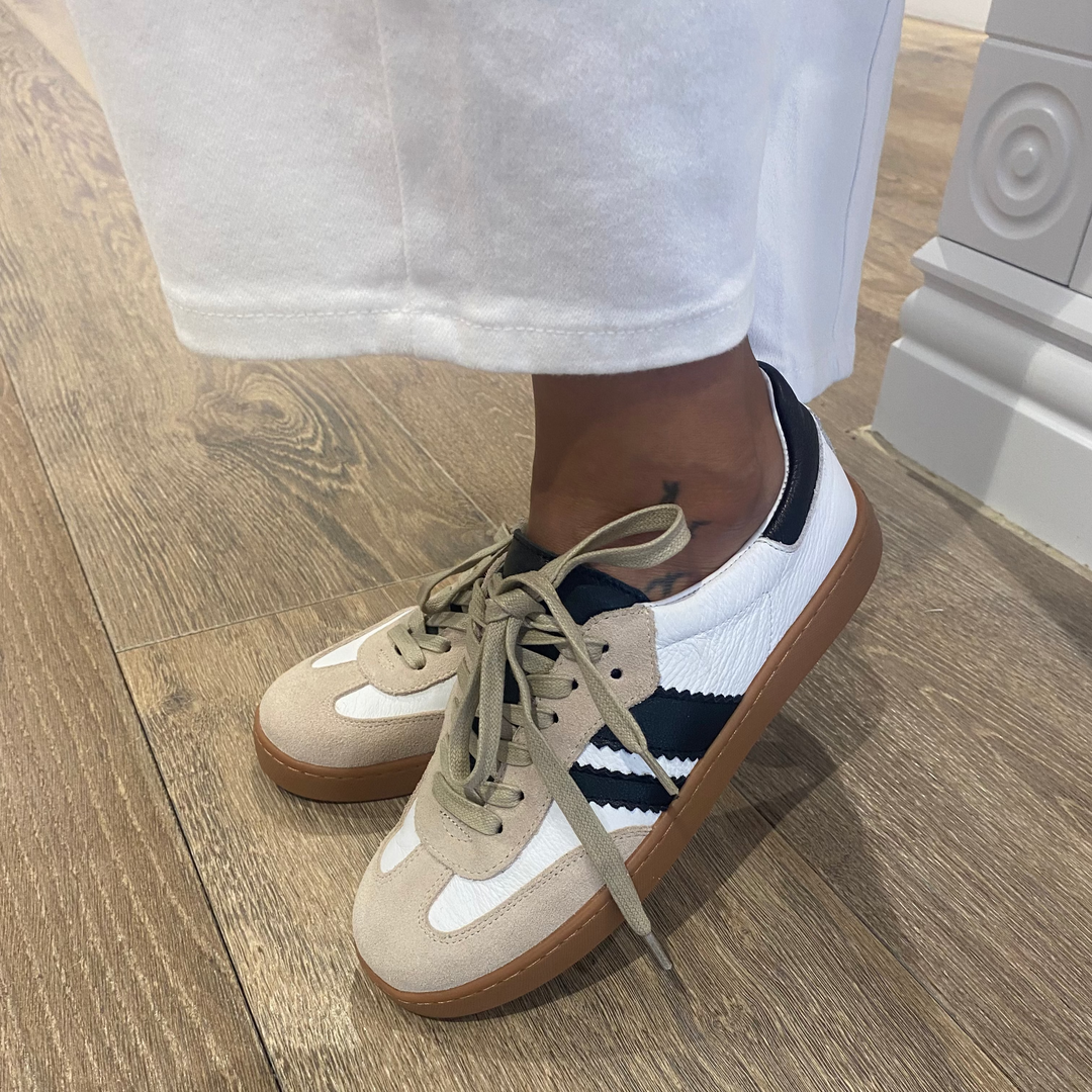 Beige sneakers with white soles worn indoors on a wooden floor.