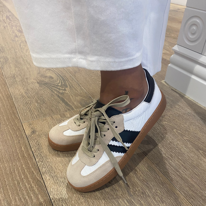 Beige sneakers with white soles worn indoors on a wooden floor.