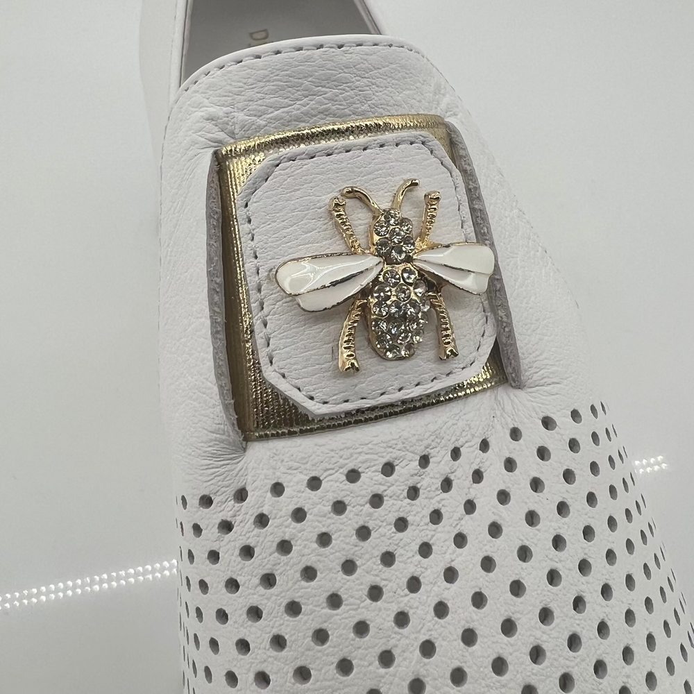 White loafer with a decorative bee pin on a light gray background