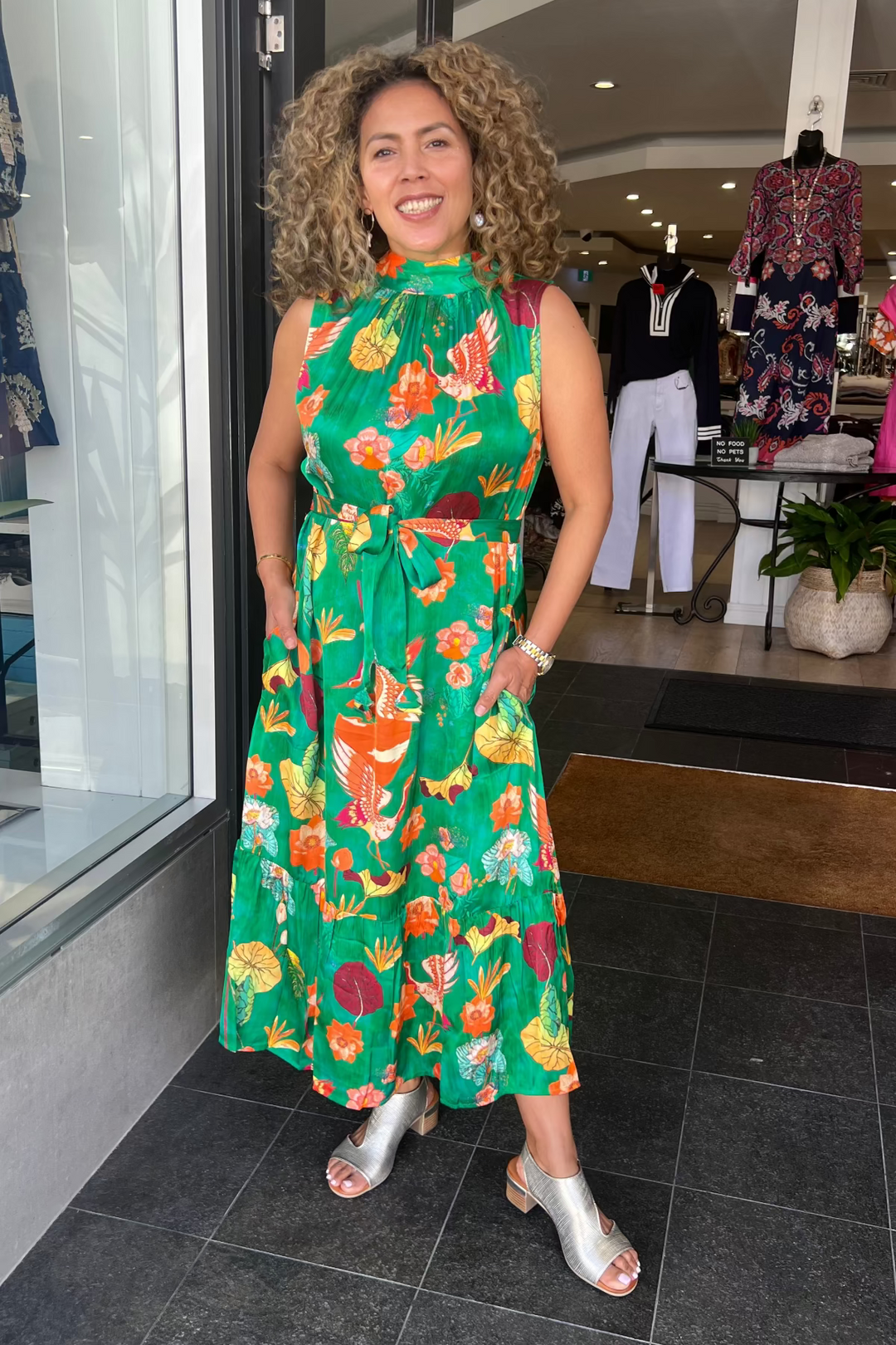 Woman in a green floral dress standing in a clothing store.