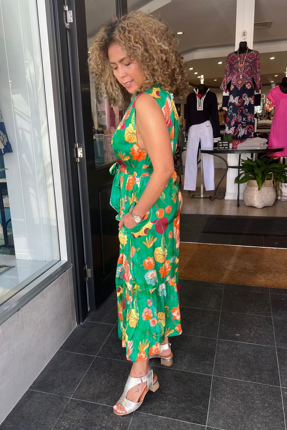 Woman in a green floral dress standing in front of a store entrance.