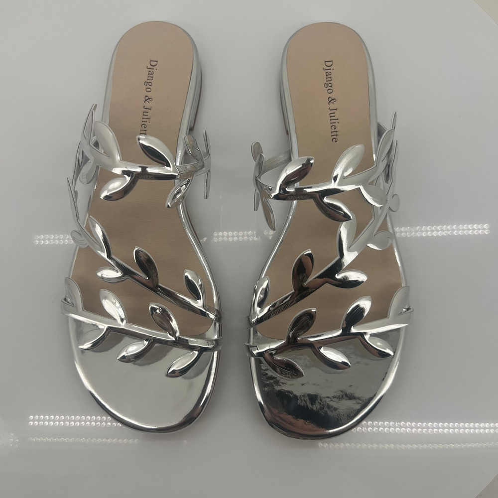 Pair of silver sandals with leaf-like designs on a white surface