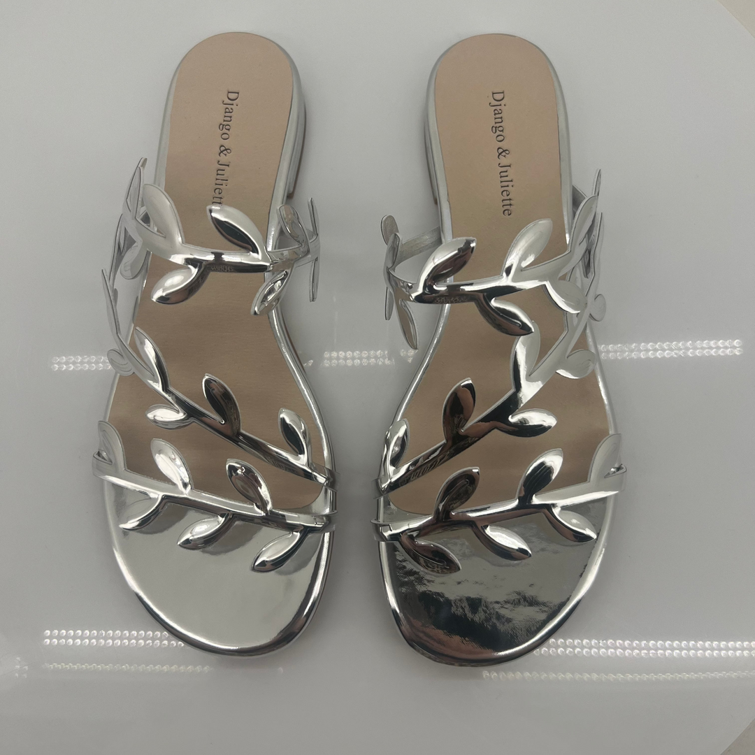 Pair of silver sandals with leaf-like designs on a white surface