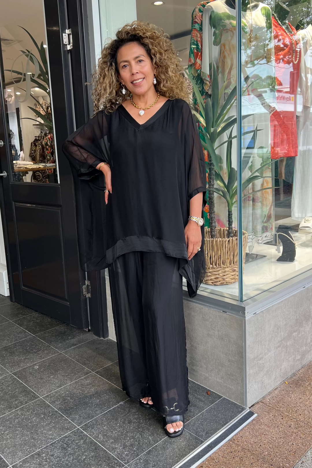 Woman in a black outfit standing outside a store with a glass door.