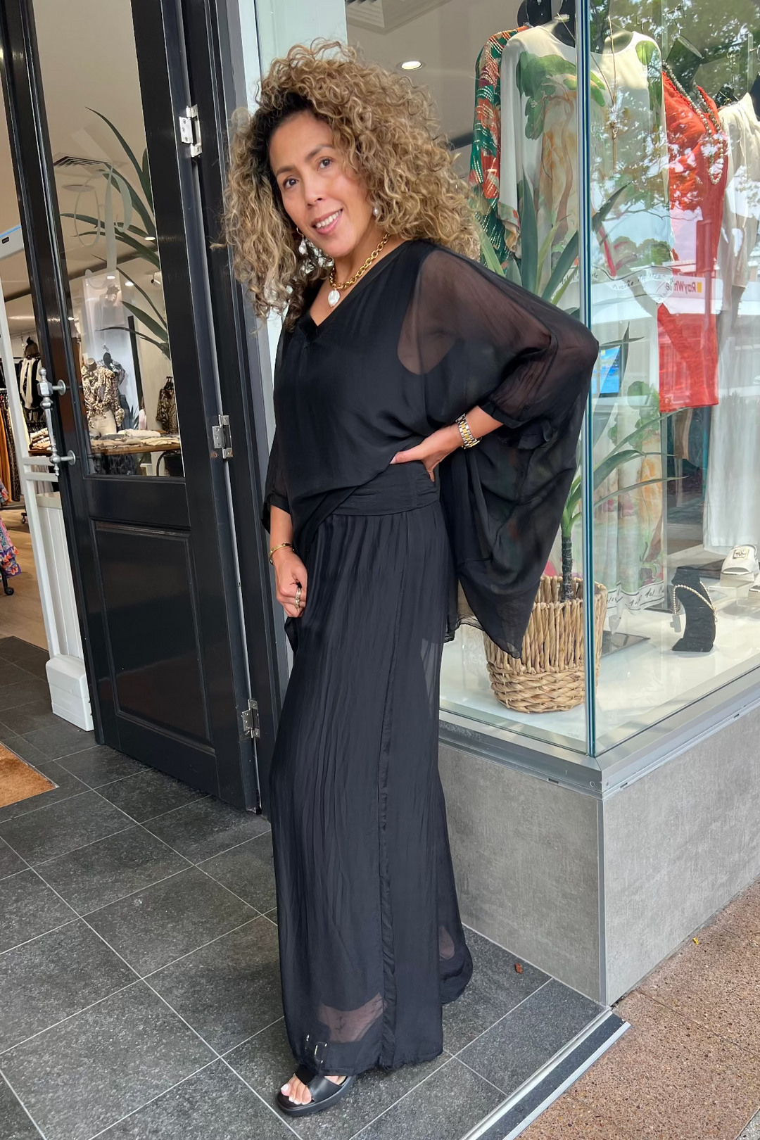 Woman in a black outfit standing outside a store with mannequins inside