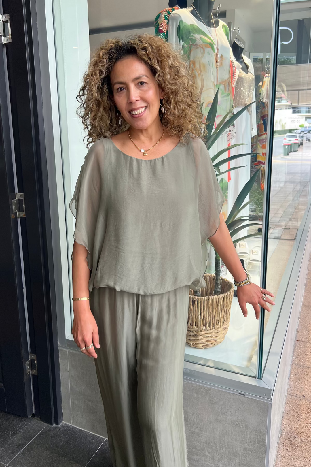 Woman standing in front of a store window wearing a light green outfit.