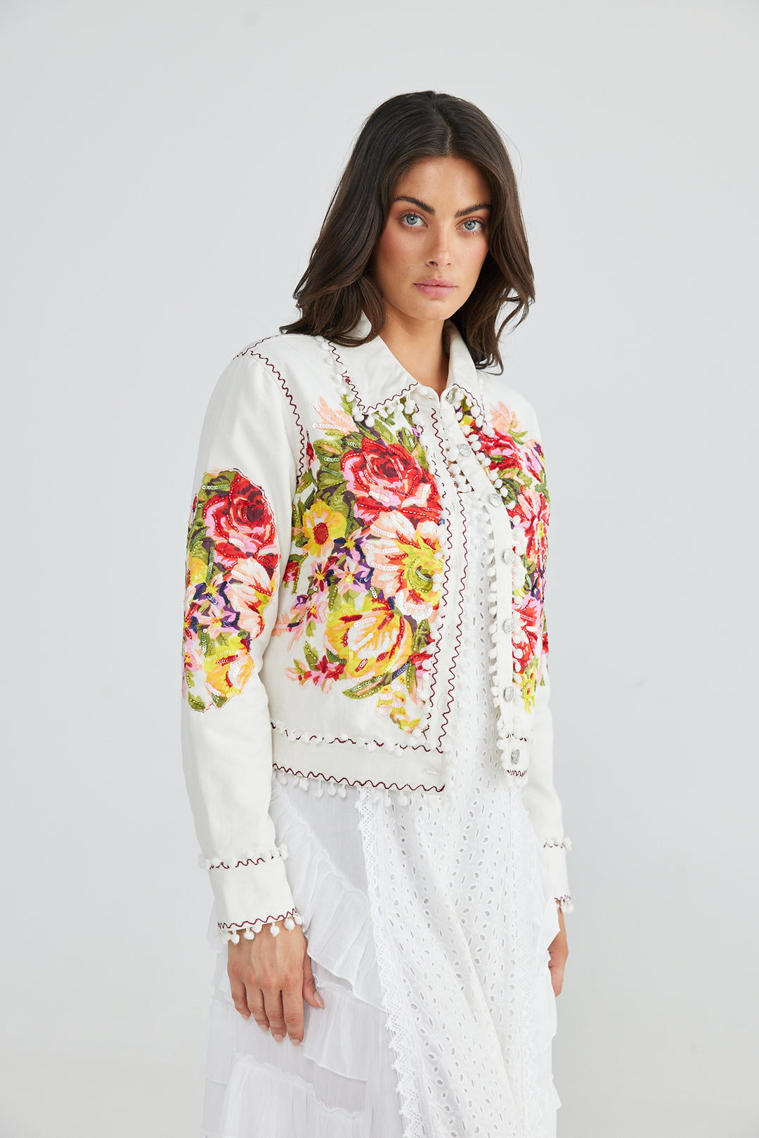Woman wearing a white jacket with floral embroidery and brown seams by Talisman, sold and shipped from Pizazz Boutique online women's clothes shops Australia