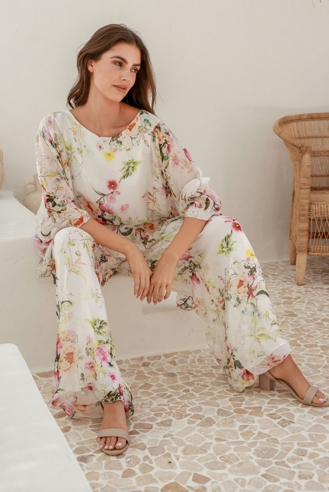 Woman wearing a pair of floral pants and a floral top by The Italian Cartel, sold and shipped from Pizazz Boutique online women's clothes shops Australia sitting down