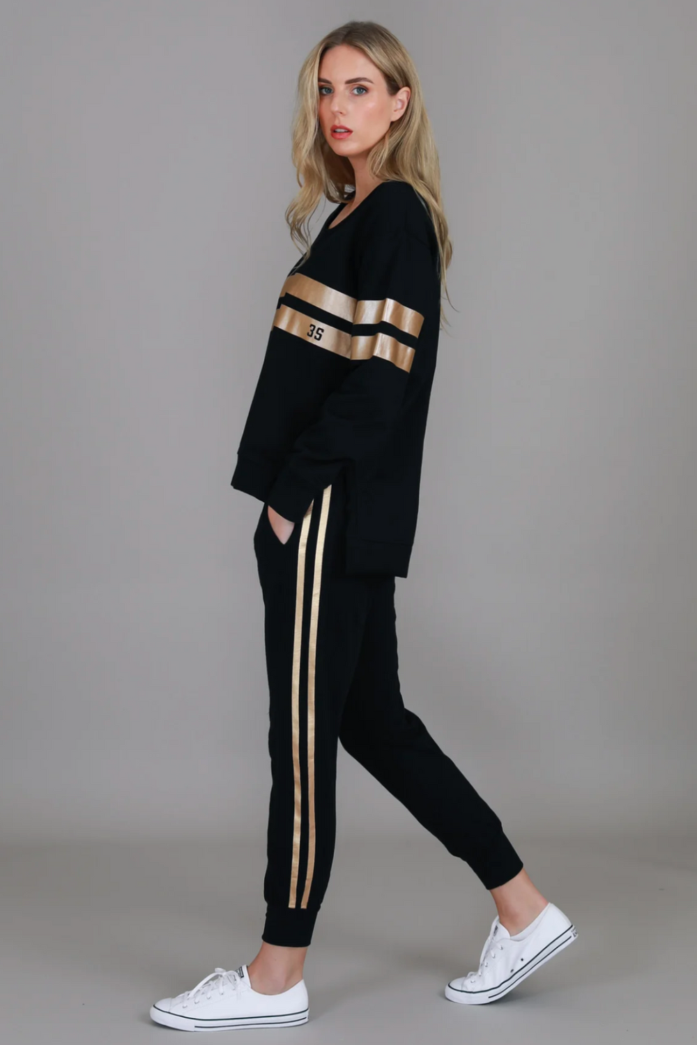 Woman wearing a black tracksuit with gold stripes on a gray background