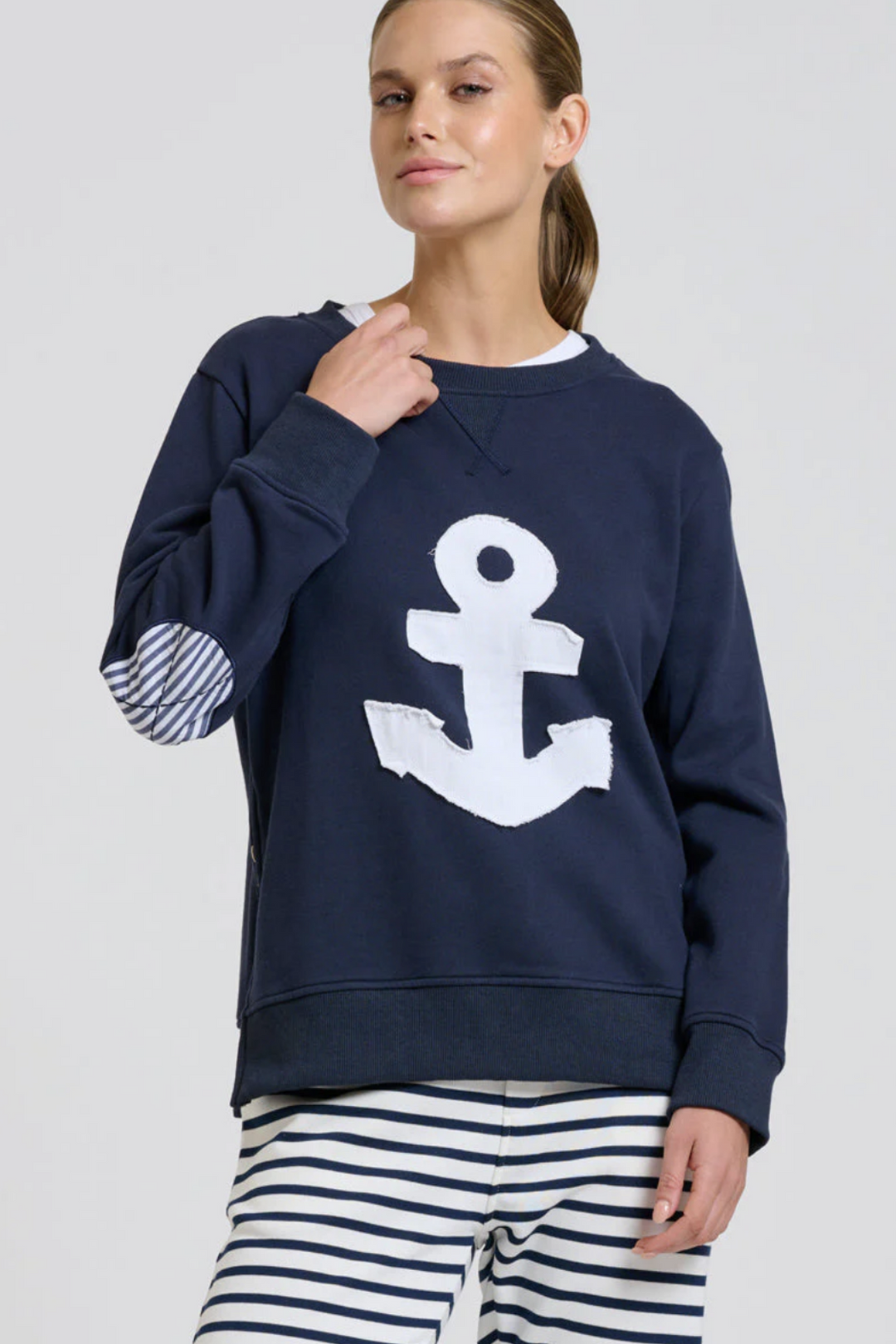 Woman wearing a navy blue sweatshirt with a white anchor design on a plain background