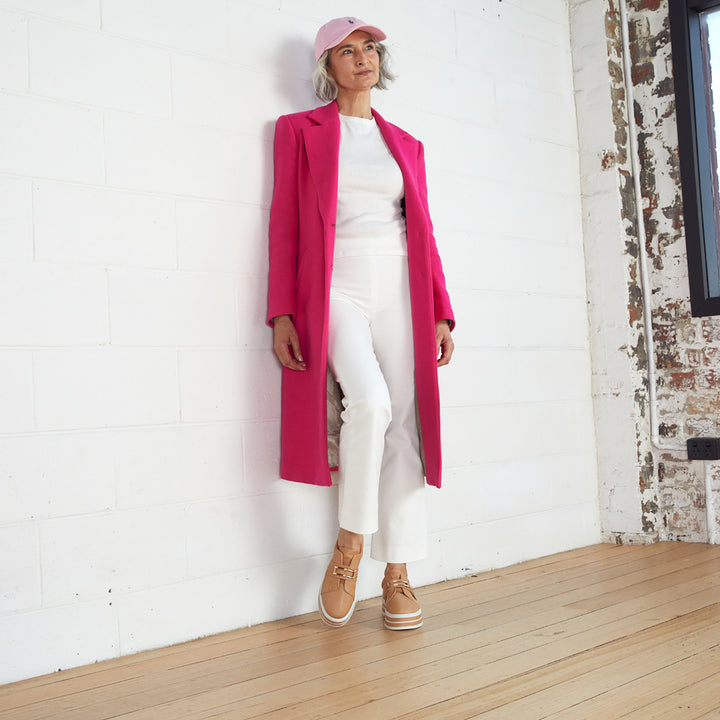 Lady in a white shirt and pants with a pink jacket wearing a light pink hat from Pizazz Boutique Nelson Bay dress shops