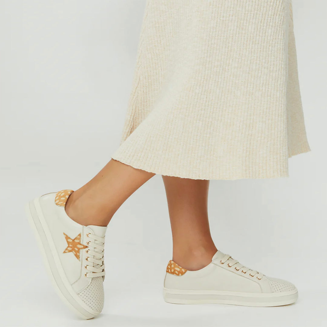 Lady wearing white sneakers with a tan star print and heel detail. Sneakers from Pizazz Boutique Nelson Bay dress shops.